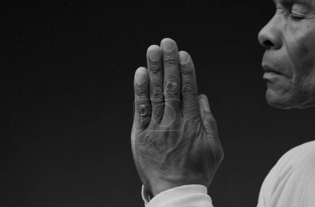 Téléchargez les photos : Homme priant Dieu avec les mains ensemble sur fond noir - en image libre de droit