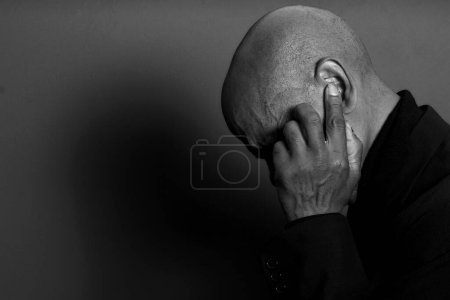 Téléchargez les photos : Homme souffrant de surdité et de perte auditive fermeture des oreilles avec les doigts sur fond sombre, noir et blanc - en image libre de droit