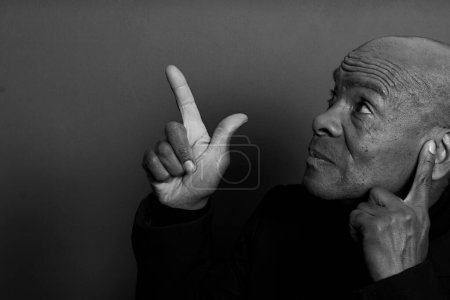 Photo for Man suffering from deafness and hearing loss closing ears with fingers and pointing on dark  background, black and white - Royalty Free Image