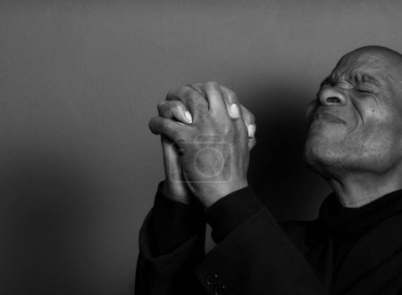 Téléchargez les photos : Homme priant Dieu avec les mains sur fond noir - en image libre de droit