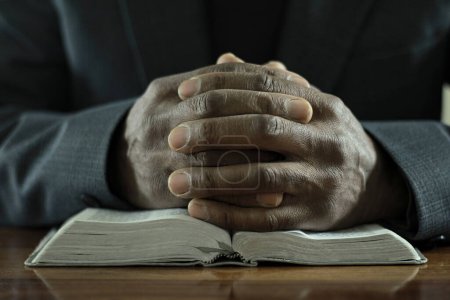Foto de Hombre rezando a Dios con la Biblia mientras está sentado en la mesa de madera, primer plano - Imagen libre de derechos