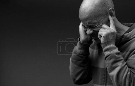 Photo for Man suffering from deafness and hearing loss closing ears with fingers on dark  background, black and white - Royalty Free Image