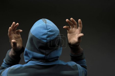 Téléchargez les photos : Vue arrière de l'homme en capuche priant Dieu avec les mains sur fond noir - en image libre de droit