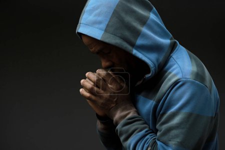 Photo for Man in hood praying to god with hands on black background - Royalty Free Image