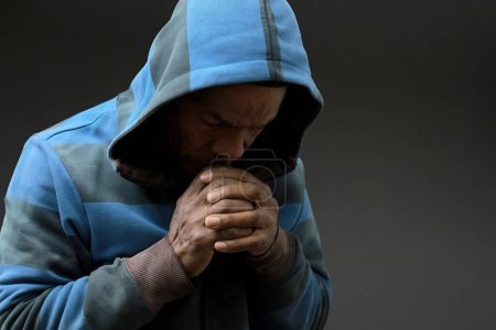 Téléchargez les photos : Homme à la cagoule priant Dieu avec les mains sur fond noir - en image libre de droit