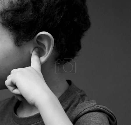 Téléchargez les photos : Portrait d'un petit garçon sourd couvrant les oreilles avec les doigts sur fond sombre en studio, noir et blanc - en image libre de droit