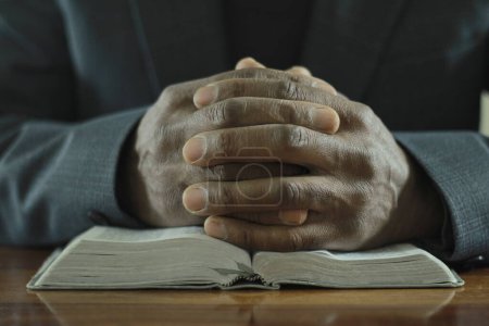 Foto de Hombre rezando a Dios con la Biblia mientras está sentado en la mesa de madera, primer plano - Imagen libre de derechos