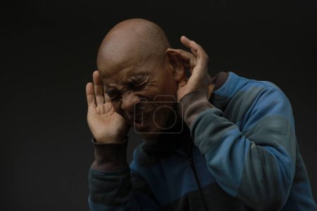 Photo for African american man suffering from deafness and hearing loss holding hands at the ears on dark background - Royalty Free Image