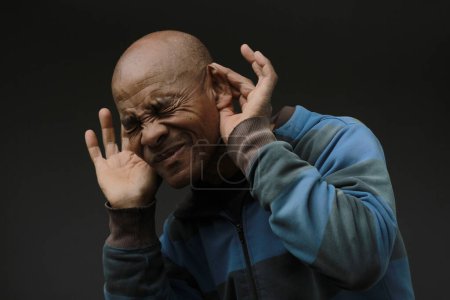Photo for African american man suffering from deafness and hearing loss holding hands at the ears on dark background - Royalty Free Image