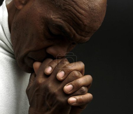 Téléchargez les photos : Homme priant Dieu avec les mains sur fond noir - en image libre de droit