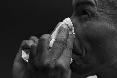 Foto de Hombre soplando la nariz después de coger un resfriado con fondo oscuro - Imagen libre de derechos