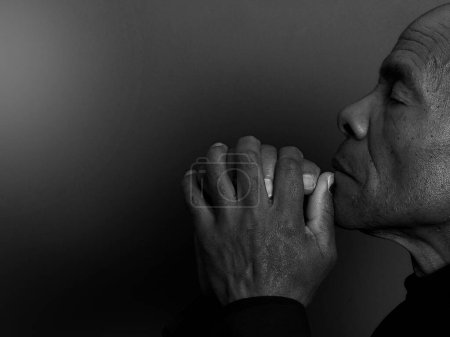 Téléchargez les photos : Homme priant Dieu avec les mains sur fond sombre - en image libre de droit