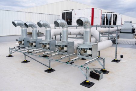 The air conditioning and ventilation system of a large industrial building is located on the roof. Large metal pipes for air duct, air conditioning, smoke removal and ventilation