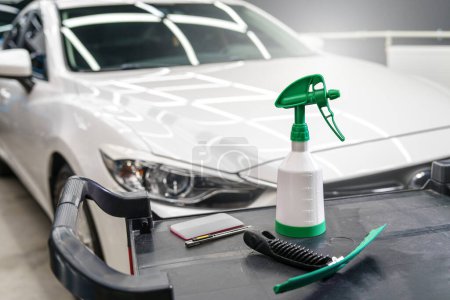 Tools for sticking protective film on the car. Universal water sprayer and special spatula on the table on the background of the car in the studio of car detailing