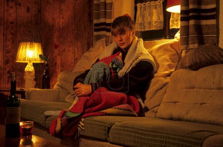 Young woman dressed warmly in the flat with blanket on the couch