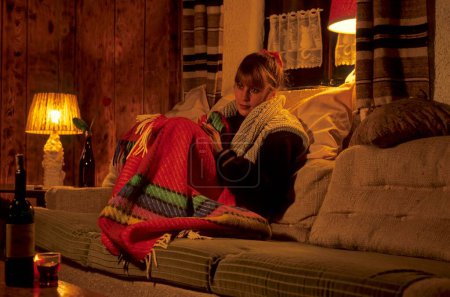 Young woman warmly dressed in the flat with blanket on the couch
