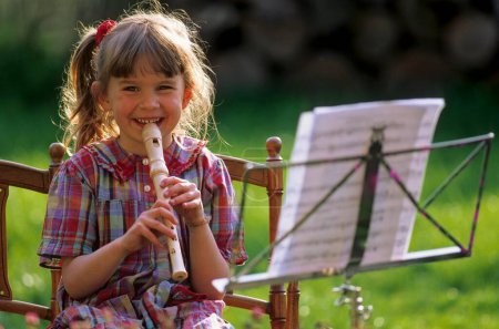 Little girl playing the flute from sheet music, music stand