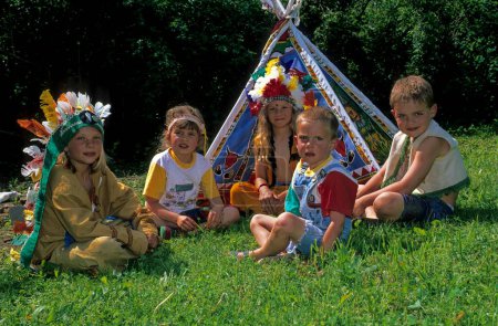 Children in a meadow with a tent playing Indians