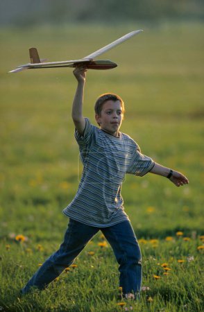 Little boy with plays with glider in a meadow