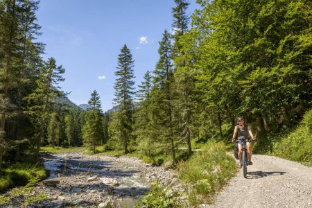 Female cyclist on a cycle path along a stream, crossing the Alps, cycle tour, Via Claudia Augusta, Upper Bavaria, Bavaria, Germany, Europe