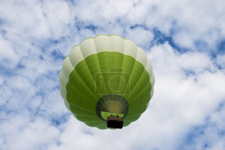 Green hot air balloon in front of blue sky with clouds, France, Europe
