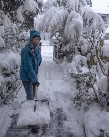 Woman with a snow shovel clearing snow, Munich, Bavaria, Germany, Europe