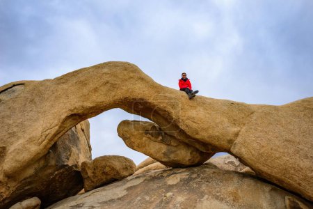 Young woman sits on Arch Rock, rock arch, monzogranite formation, Arch Rock Nature Trail