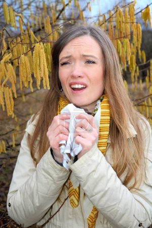 Mujer con alergia al polen entre avellanos florecientes (Corylus), Scania, Suecia, Europa