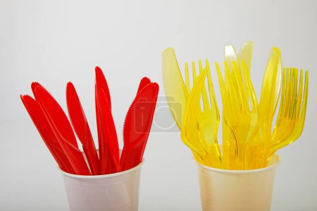 Cubiertos de plástico rojo y amarillo en vasos de plástico, cuchillos de plástico, tenedores de plástico, residuos de plástico
