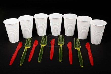 Cubiertos de plástico rojo y amarillo, cuchillos de plástico, tenedores de plástico, vasos de plástico blanco, residuos de plástico