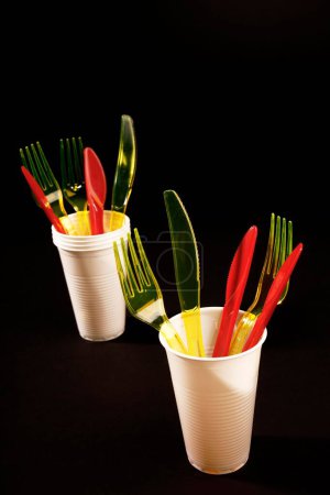 Cubiertos de plástico rojo y amarillo en vasos de plástico blanco, cuchillos de plástico, tenedores de plástico, basura de plástico