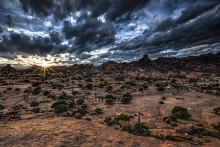 Small village of Aguard Oudad with brightly painted houses in front of the rock Chapeau Napoleon, dramatic clouds, evening, Tafraoute, Anti Atlas, Southern Morocco, Morocco, Africa