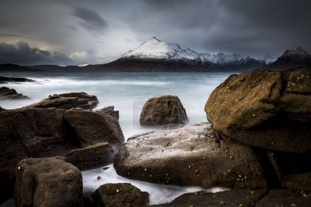 Große Felsen im Wasser der Nordsee mit schneebedeckten Cullin-Bergen im Hintergrund, Elgol, Isle of Skye, Schottland, Großbritannien, Europa