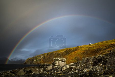 Große Felsen im Wasser der Nordsee mit schneebedeckten Cullin-Bergen und Regenbogen im Hintergrund, Elgol, Isle of Skye, Schottland, Großbritannien, Europa