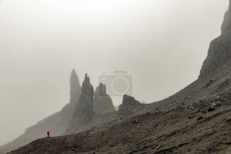 Rock Old Man of Storr with tourist with red umbrella in fog, Portree, Isle of Sky, Scotland, Great Britain