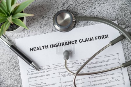 Téléchargez les photos : Top view of doctor's stethoscope, pen and health insurance claim form on table - en image libre de droit