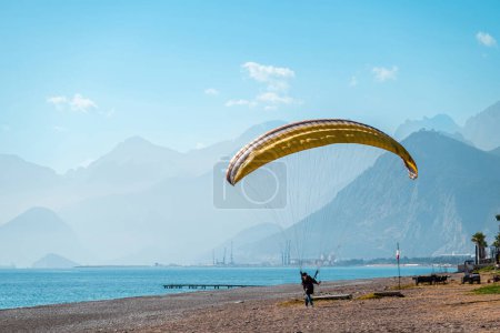 Foto de Man practicing paragliding on a windy day on the beach by the sea - Imagen libre de derechos