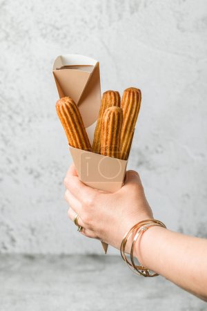 Photo for Woman taking churros from a cone and dipping it in chocolate sauce - Royalty Free Image
