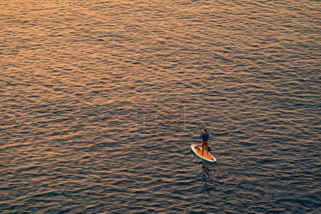 Photo for Adventurous people on a stand up paddle board is paddling during a bright and vibrant sunrise - Royalty Free Image