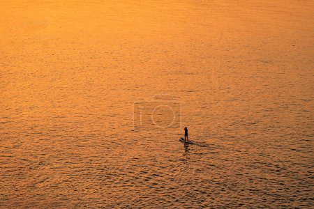 Foto de Gente aventurera en una tabla de remo de pie está remando durante un amanecer brillante y vibrante - Imagen libre de derechos