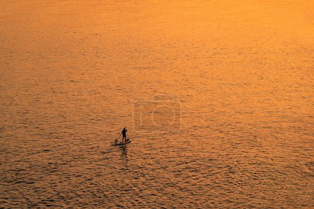 Photo for Adventurous people on a stand up paddle board is paddling during a bright and vibrant sunrise - Royalty Free Image