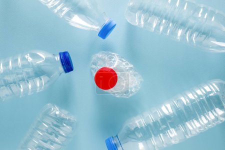 Foto de Botellas de agua plásticas trituradas con tapas azules alrededor de la botella de agua plástica triturada con tapa roja sobre fondo azul - Imagen libre de derechos