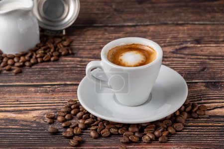 Espresso macchiato w białej porcelanowej filiżance z mlekiem i ziarnem kawy na drewnianym stole