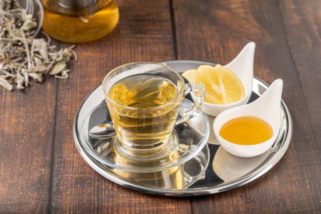 Photo for Dried sage tea in glass cup on wooden table - Royalty Free Image