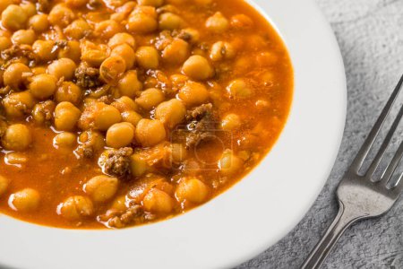 Chickpea stew with minced meat on a white porcelain plate on a stone table