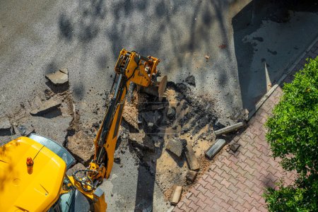Excavadora excavando asfalto para reparar una falla de agua en una calle