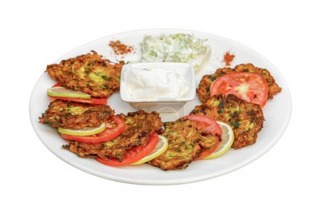 Zucchini hash or Turkish kabak mucver with yoghurt and tomatoes on a white plate