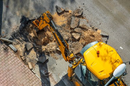 Digger digging asphalt to repair a water fault in a street