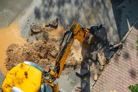 Photo for Digger digging asphalt to repair a water fault in a street - Royalty Free Image