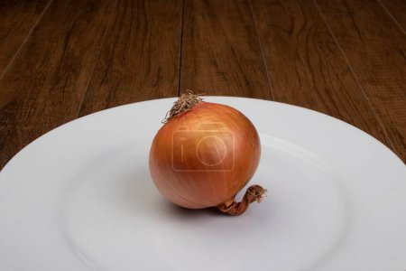 Foto de Cebolla cruda sin pelar en plato blanco sobre mesa de madera. - Imagen libre de derechos